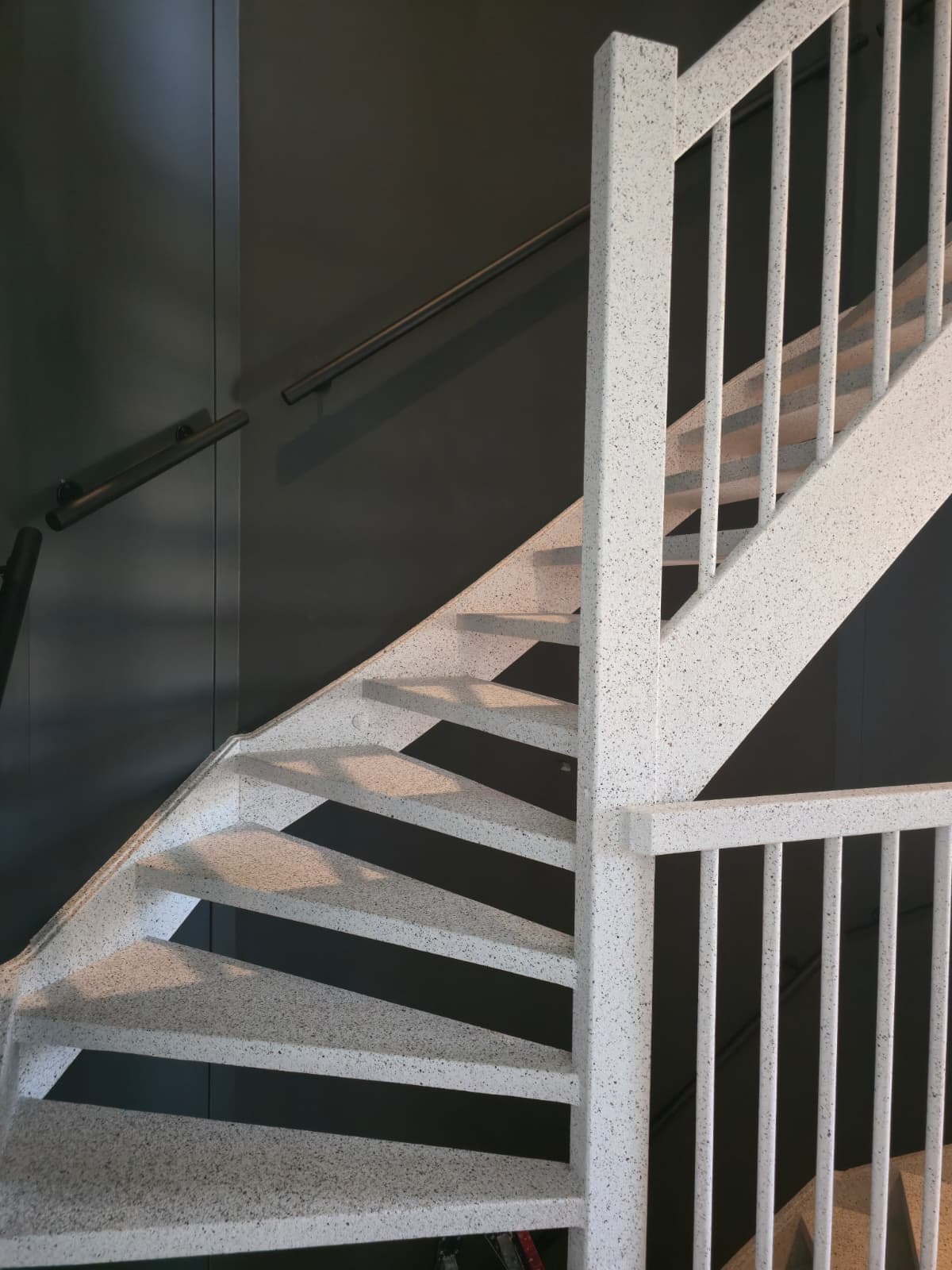 Signature stair renovation — open staircase in white terrazzo against a dark wall